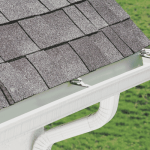Alt Text: Beige residential house with asphalt shingle roof and white gutter system under a clear blue sky